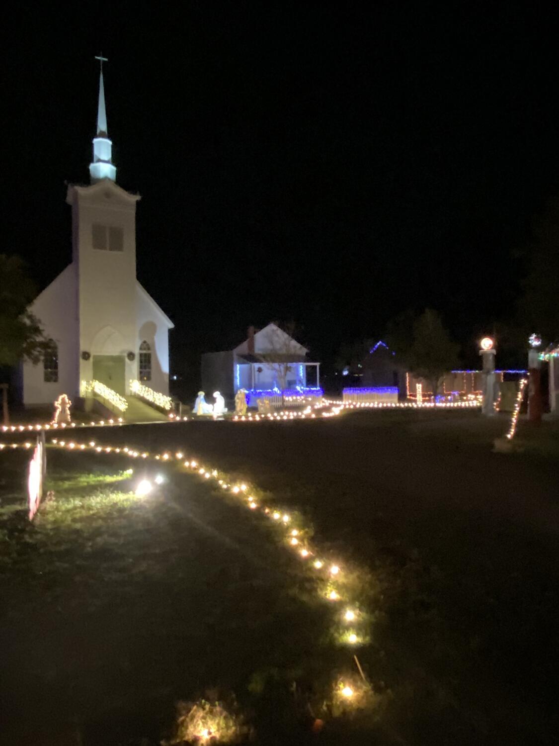 The white country church in the Heritage Village lit up at night with a lighted path